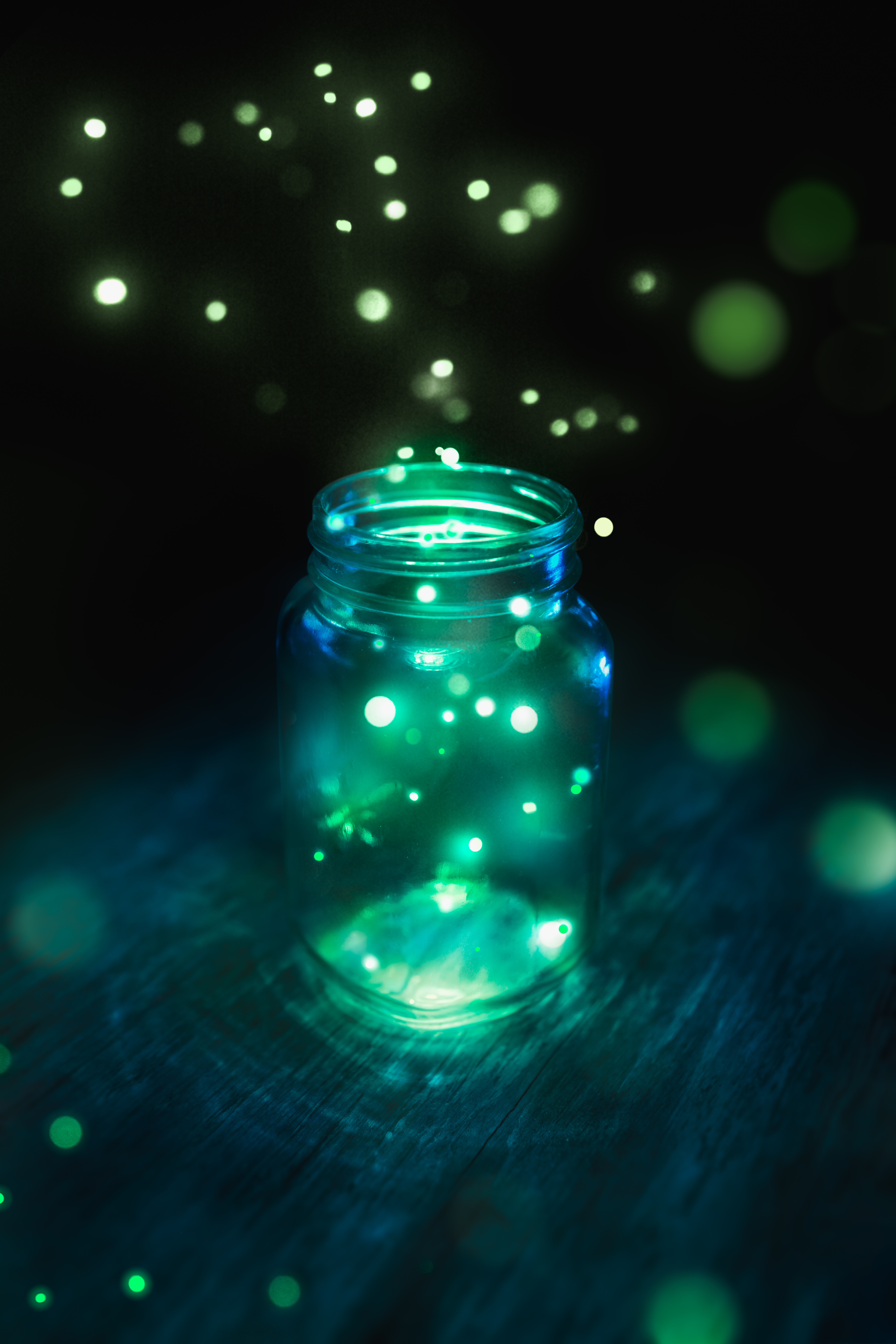 Fireflies captured in a jar on a dark wood background at night